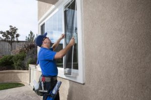 Man cleaning window of a home and installing a screen,